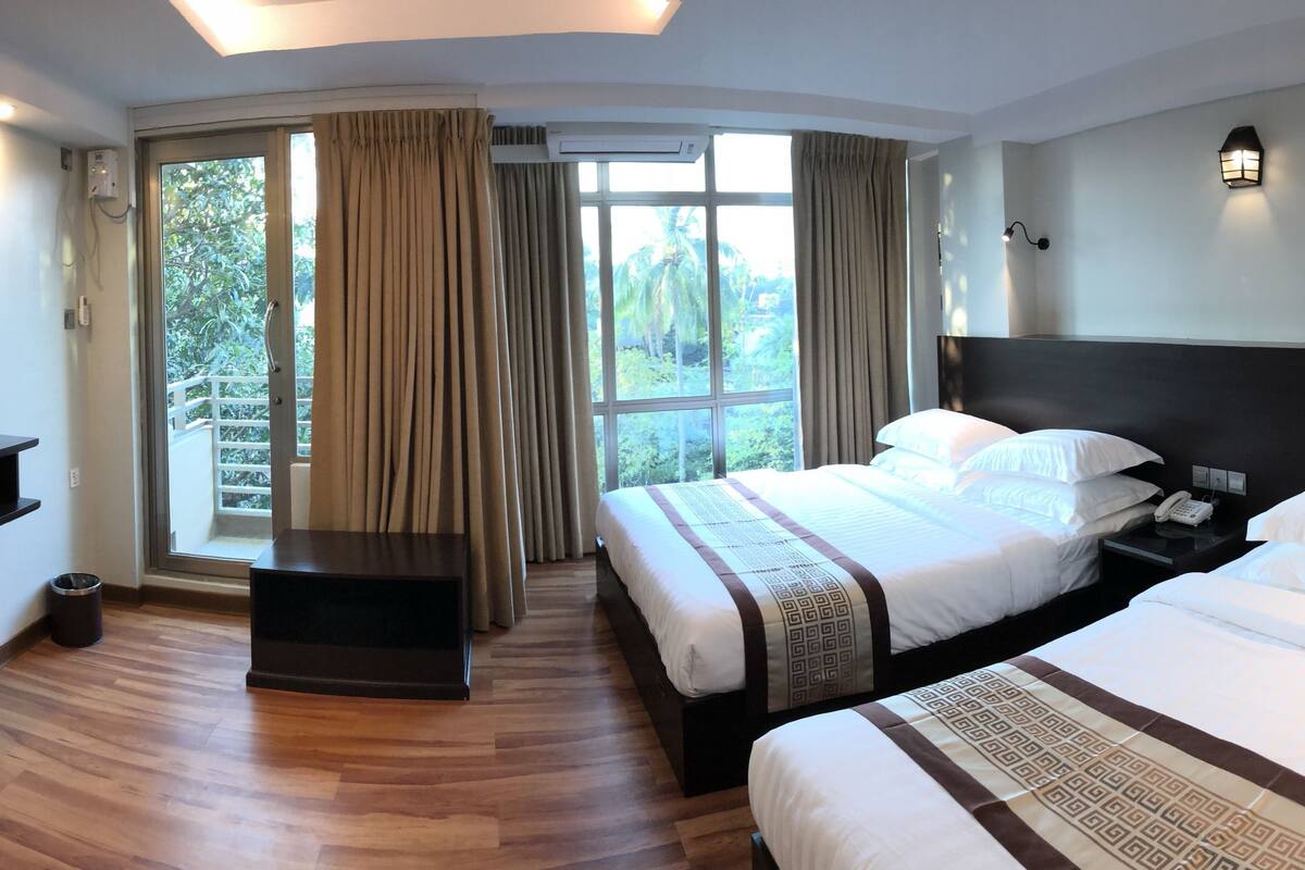 A hotel room with two beds, a TV, a desk, and a window with curtains.