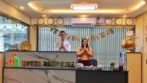 A hotel reception desk with clocks, a floral arrangement, and a sign reading "HOTEL ROSE HILL." - Hotel Rose Hill (Yangon)