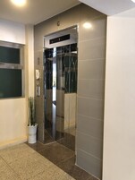 Un ascensor con pantalla digital, una planta en maceta y piso de baldosas.