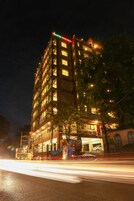 Un hotel de varios pisos con señalización iluminada, un estacionamiento visible y una calle con estelas de luz.