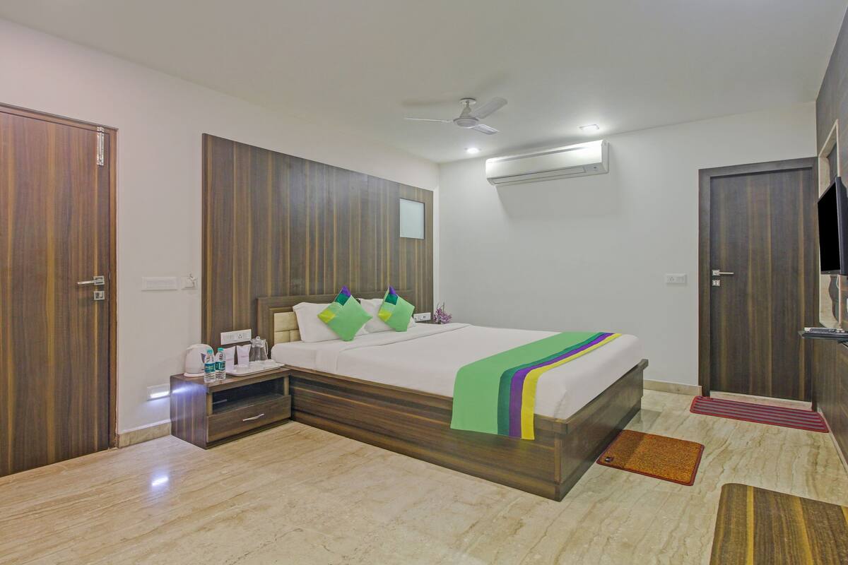 A hotel room with a wooden bed, a ceiling fan, an air conditioner, and a TV.