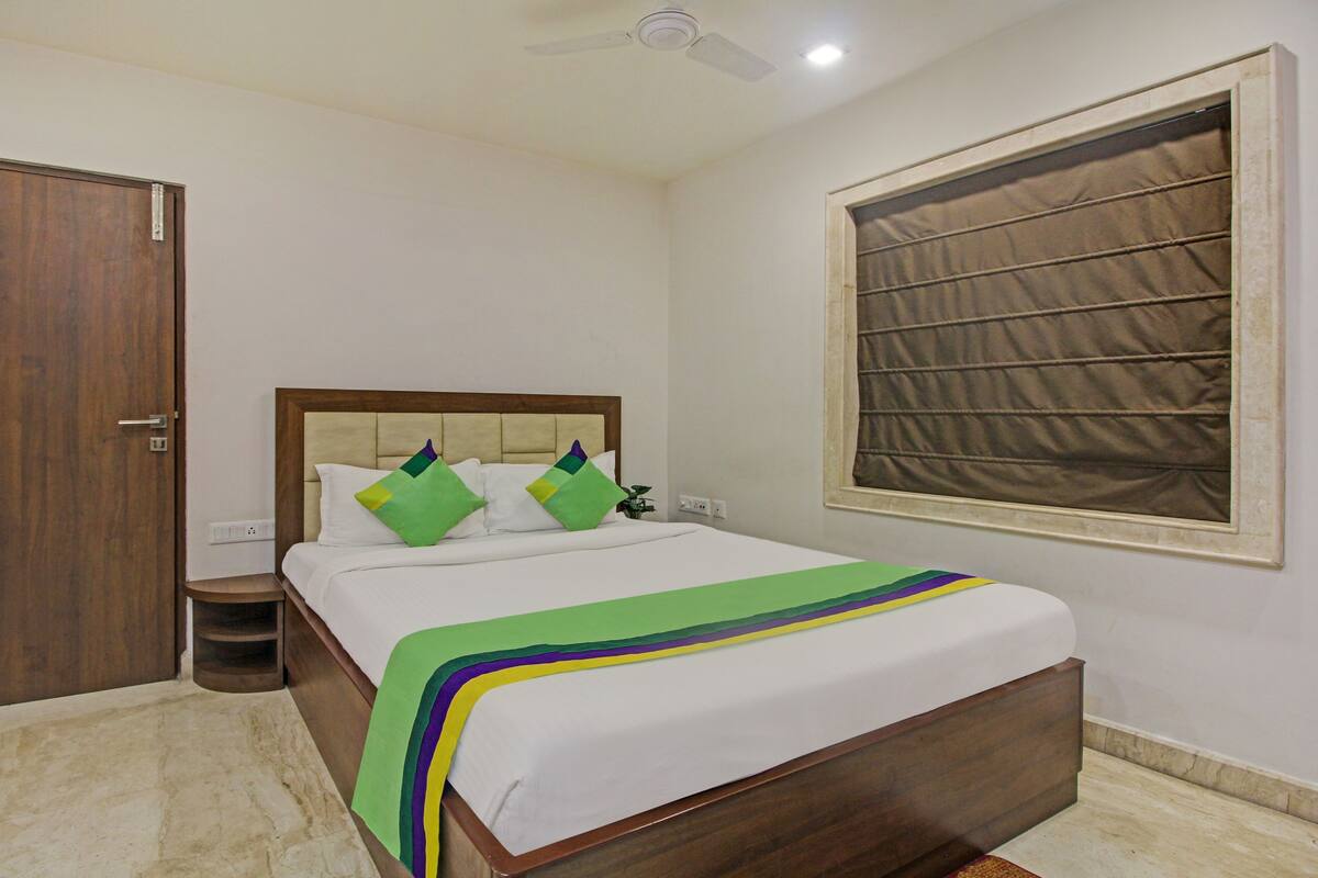 A bedroom with a wooden bed, a nightstand, a ceiling fan, a window with blinds, and a door.