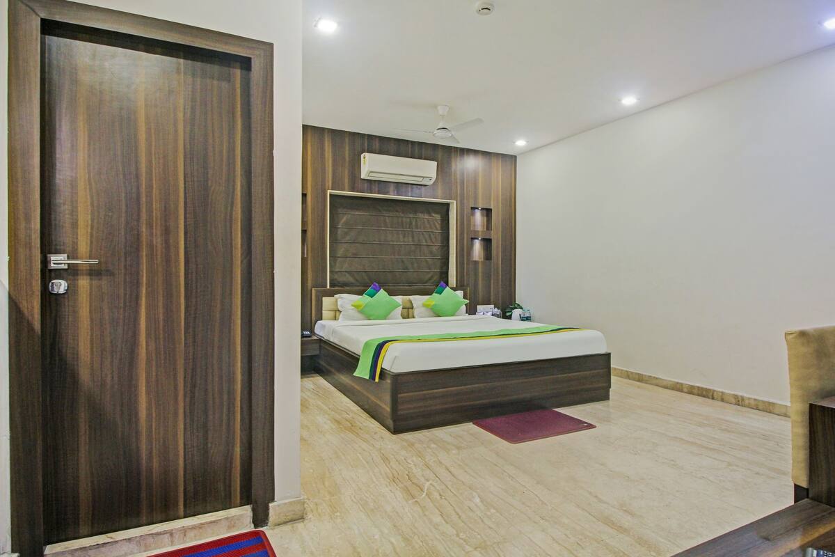 A hotel room with a wooden door, a bed with a green and white bedspread, a ceiling fan, and an air conditioning unit.
