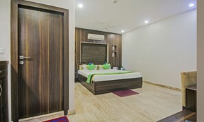 A hotel room with a wooden door, a bed with a green and white bedspread, a ceiling fan, and an air conditioning unit. - Treebo Sreema Saltlake Near City Centre Mall (Bidhannagar)