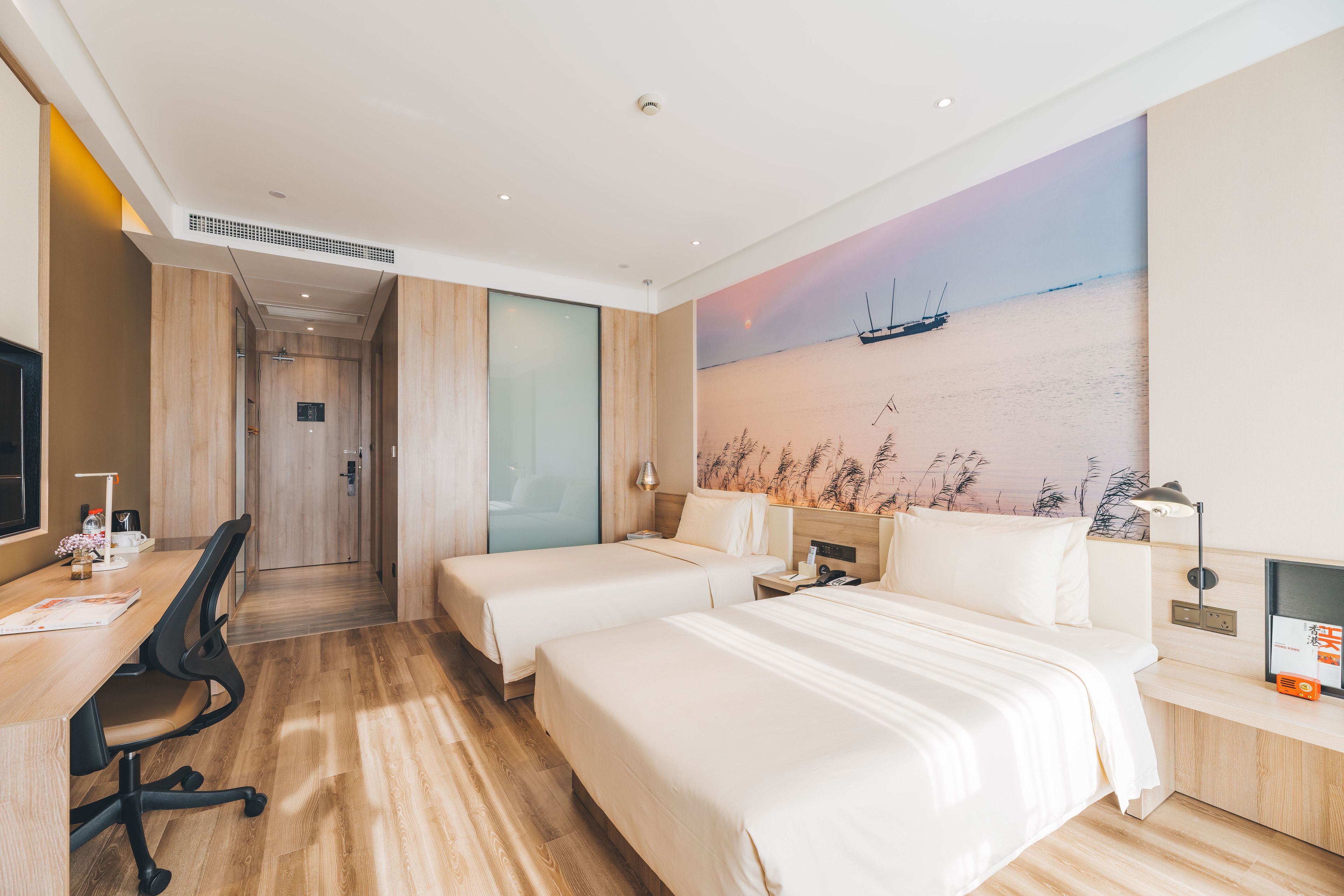 A hotel room with two beds, a desk, and a chair. There is a painting of a boat on the wall.