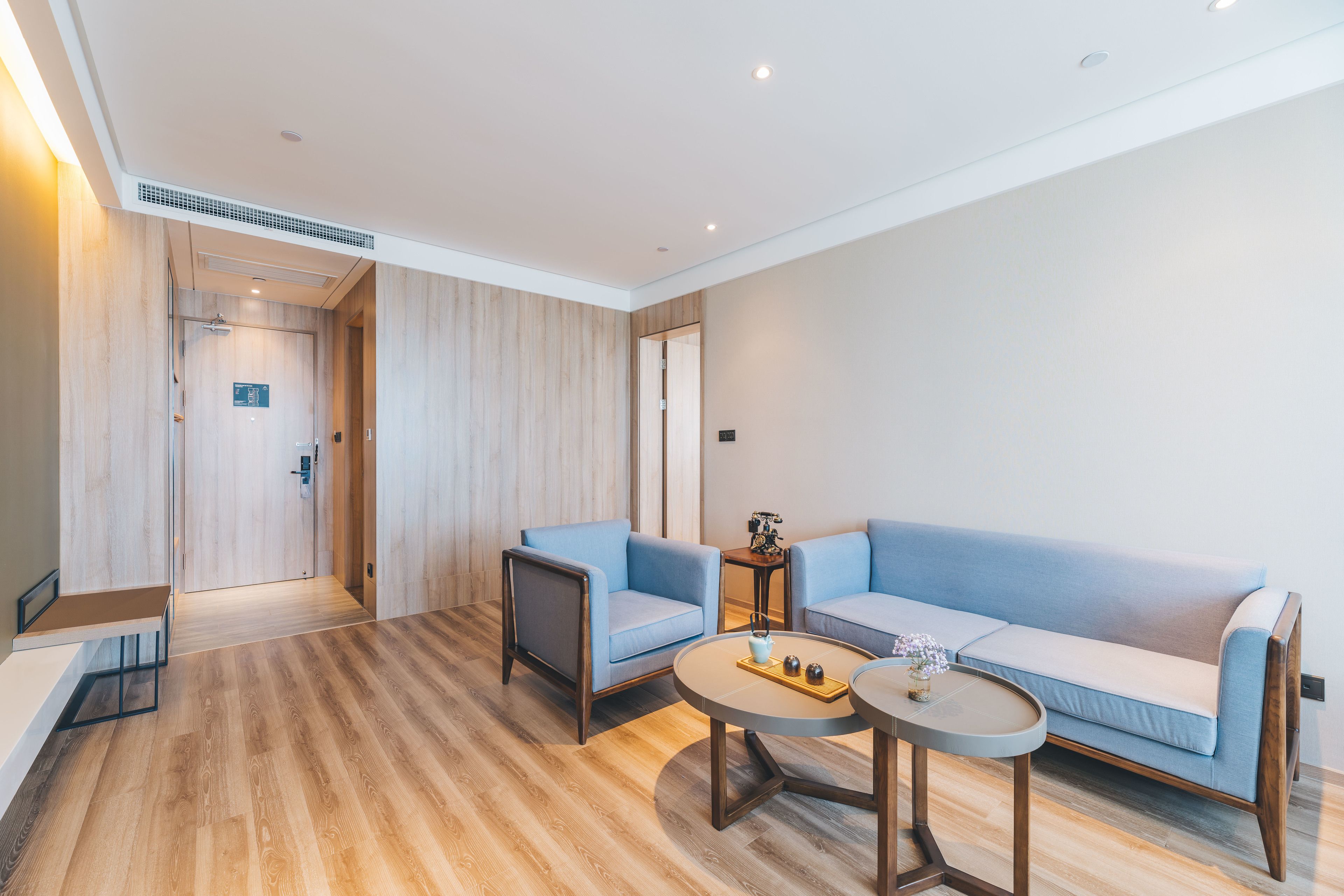 Une chambre d’hôtel moderne avec un plancher en bois, un canapé bleu clair, une petite table ronde et un banc en bois.
