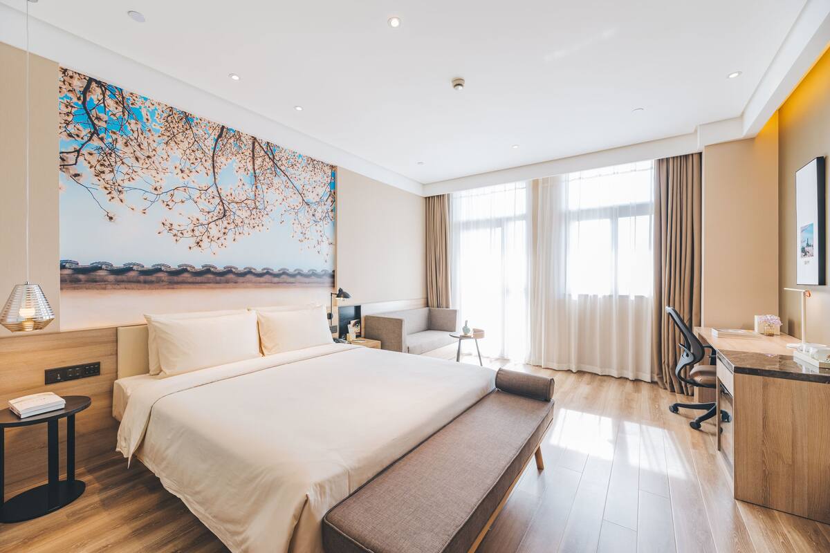 A modern hotel room with a large bed, a desk, a chair, and a sofa.