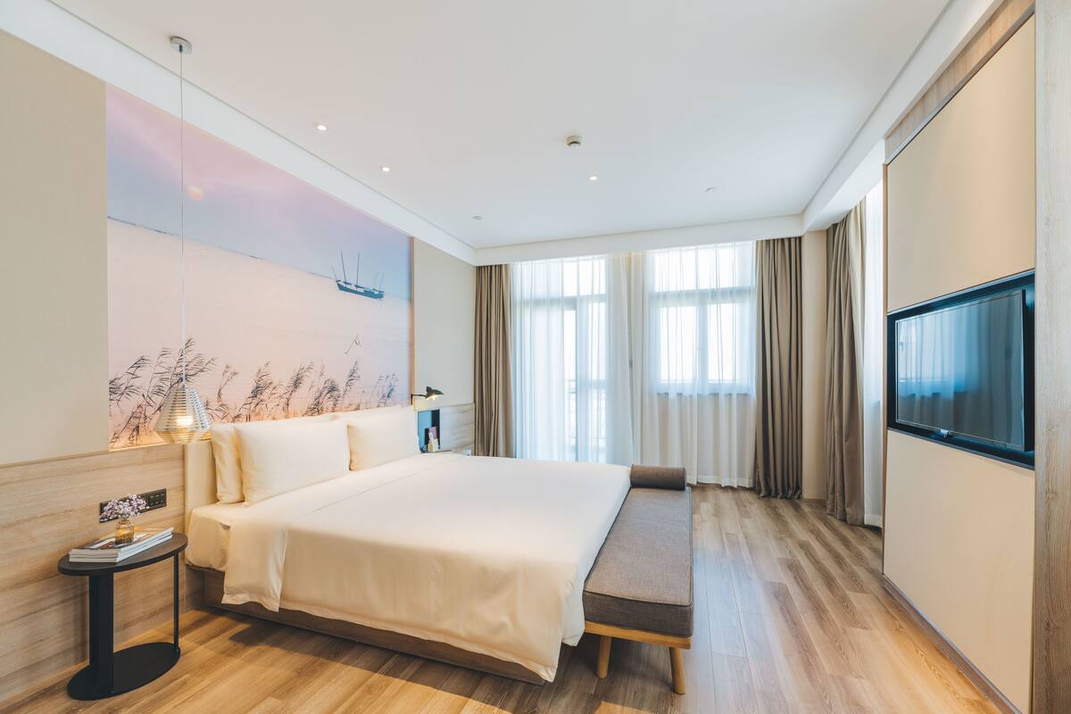 A modern hotel room with a large bed, a sofa, a TV, and a wall-mounted artwork.