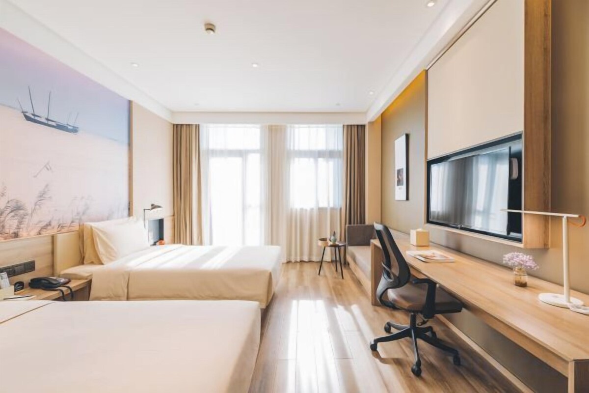 A hotel room with two beds, a desk, a TV, and a large window.