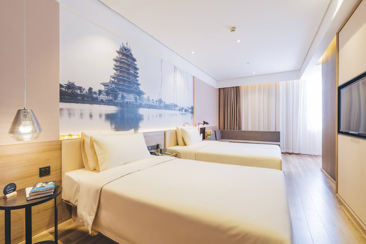 A hotel room with two beds, a large wall mural, a TV, and a small table with a lamp.