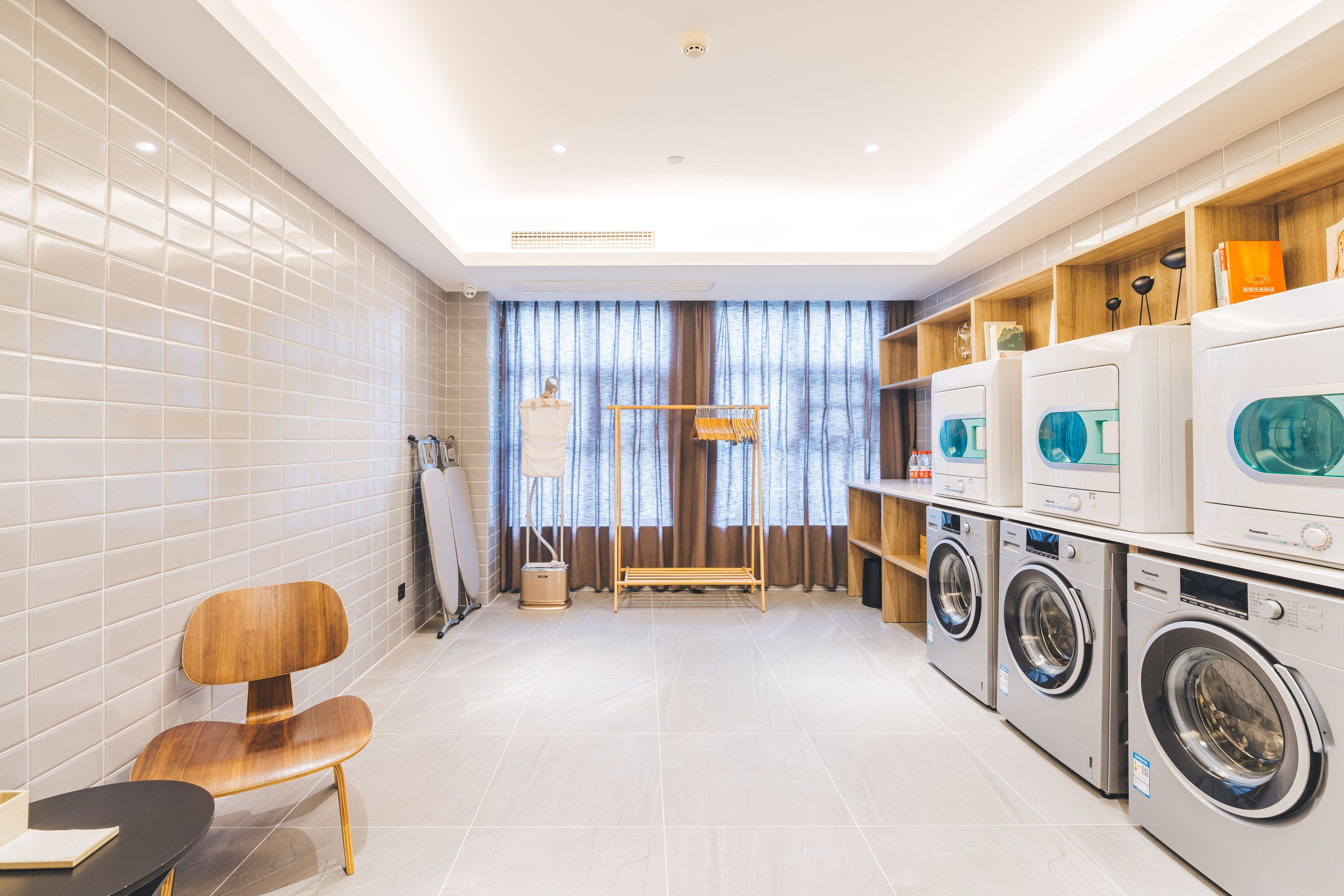 A modern laundry room with a washing machine, dryer, and a chair.
