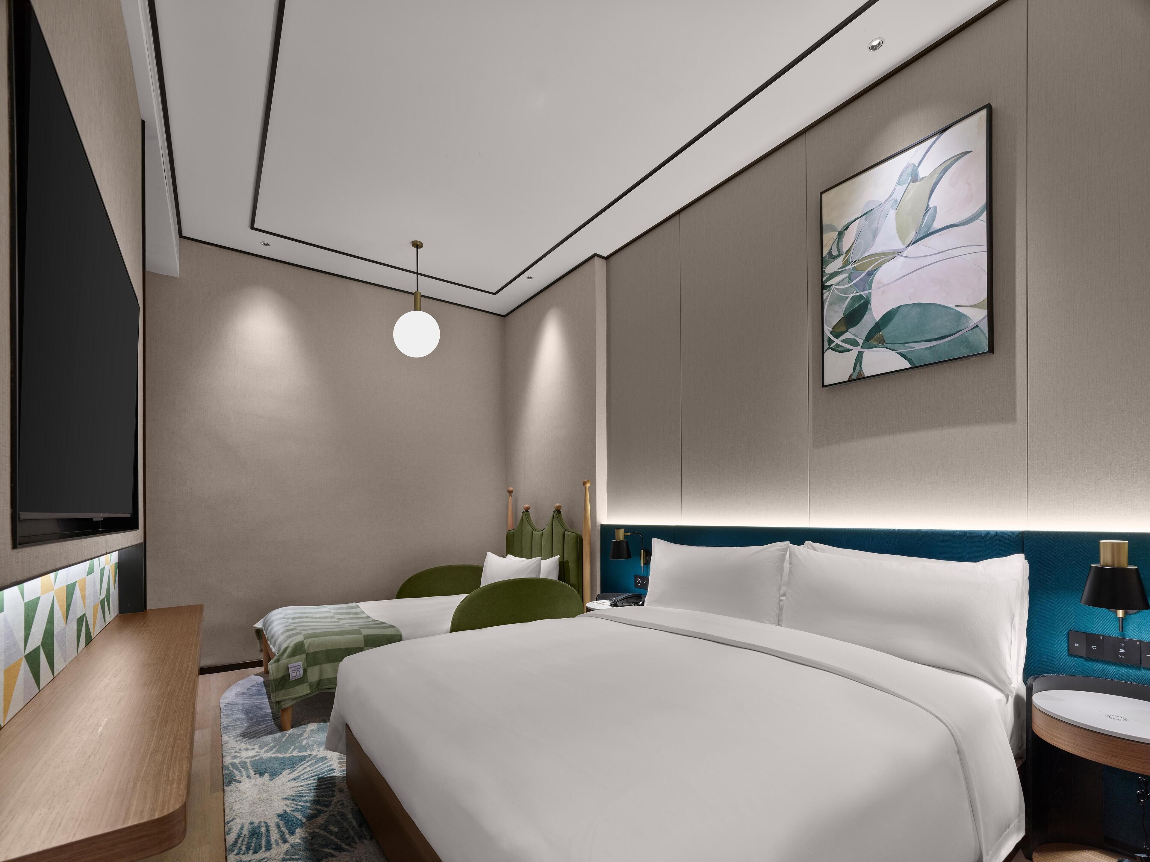 A modern hotel room with a large bed, two smaller beds, a desk, and a TV.