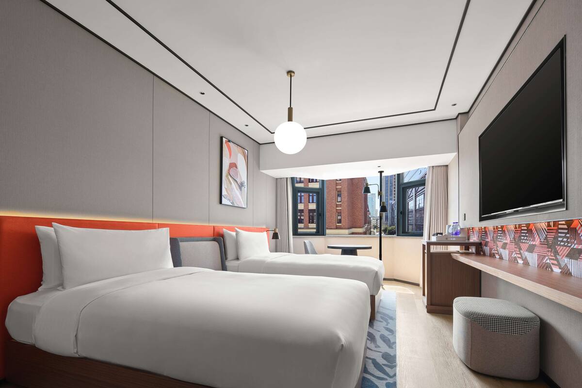 Habitación de hotel moderna con dos camas, un escritorio, un televisor y vistas a la ciudad.