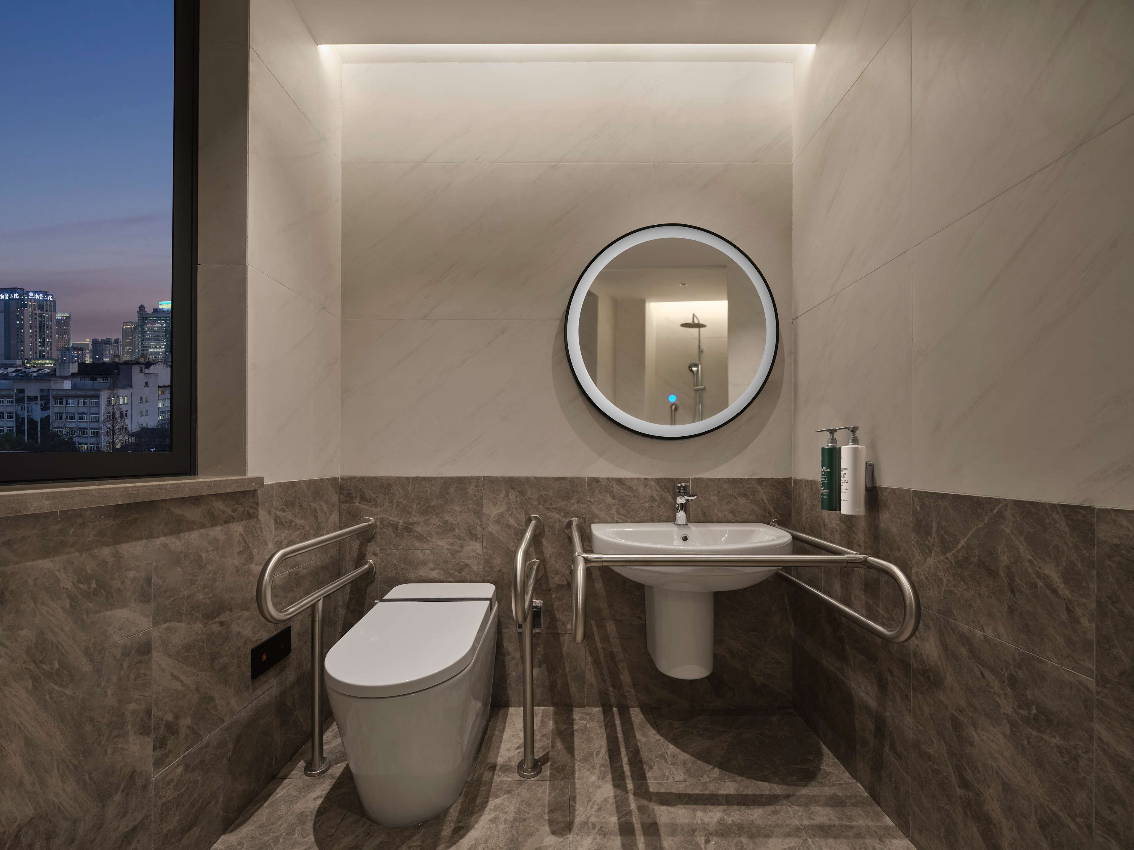 Un baño moderno con inodoro, lavamanos y barras de apoyo.
