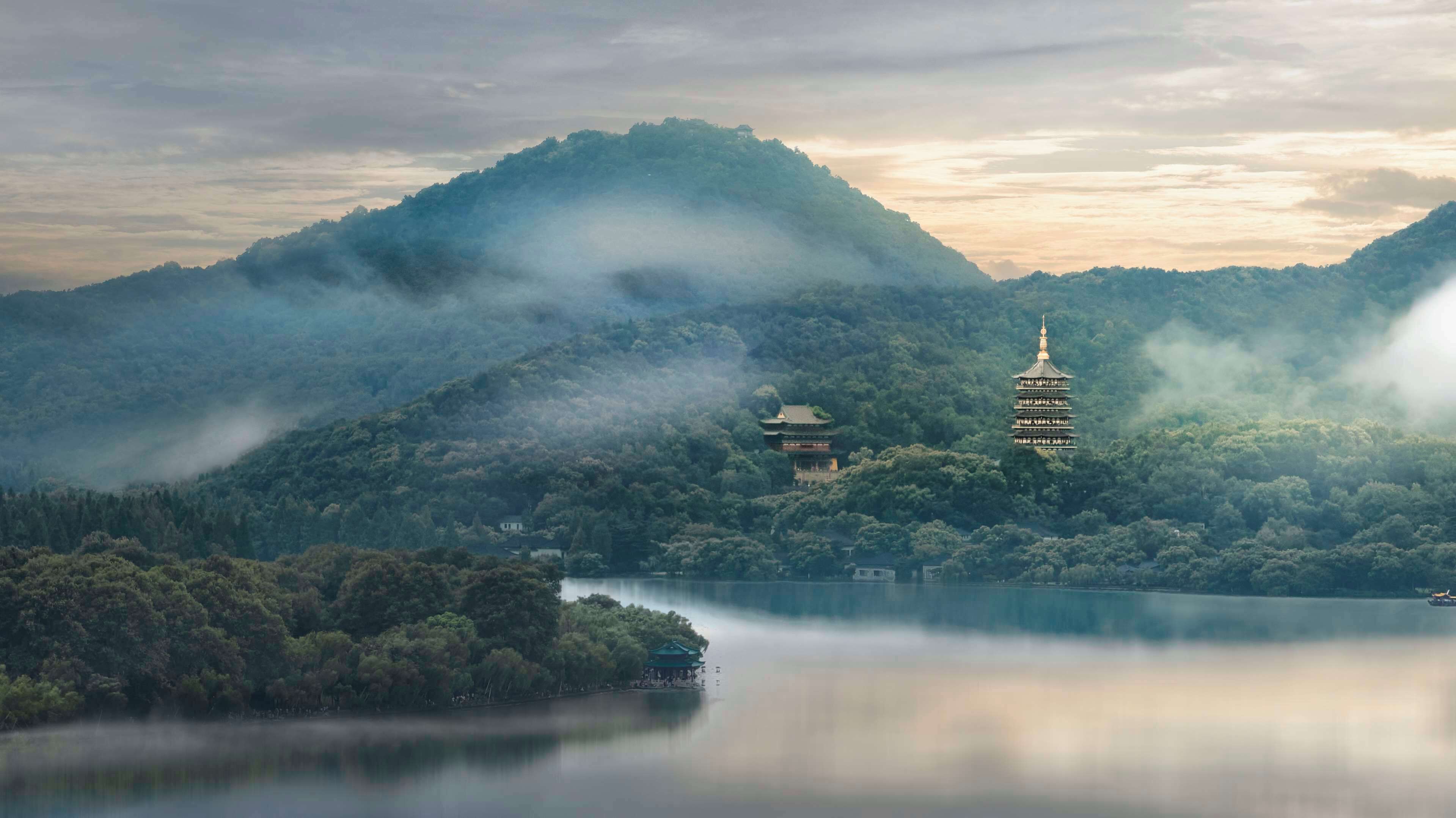 A serene landscape with a pagoda on a hill, surrounded by lush greenery and a calm lake.