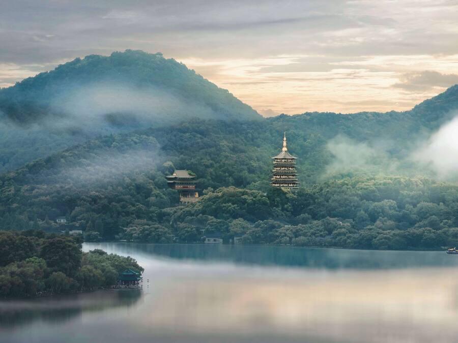 Un paisaje sereno con una pagoda en una colina, rodeado de vegetación exuberante y un lago tranquilo.