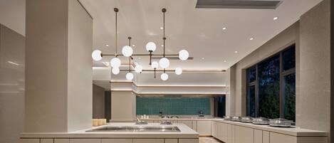 A modern kitchen with a central island, pendant lighting, and a view of the outdoors through large windows.