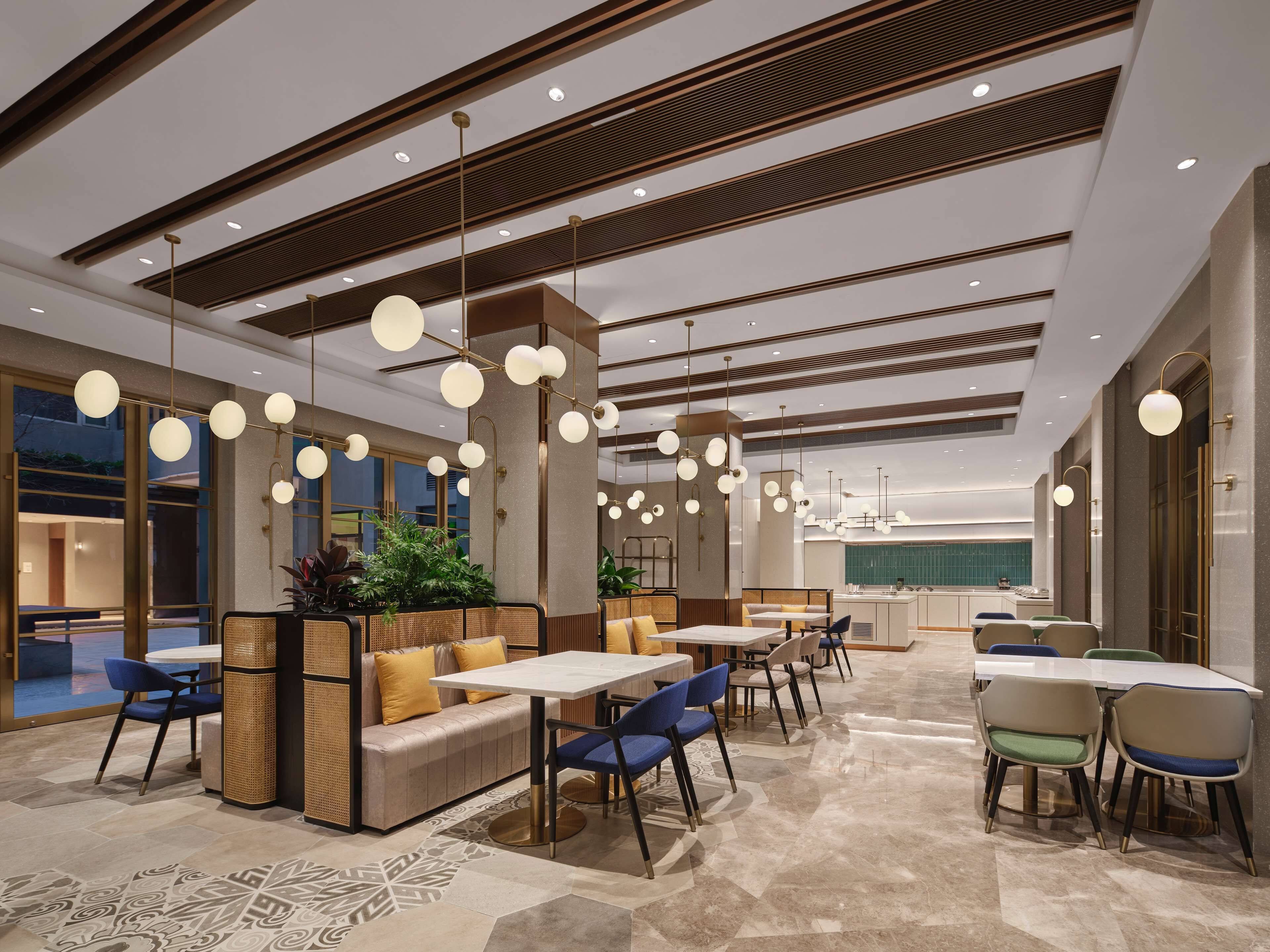 Un moderno hall de hotel con zonas de estar, mesas y una cocina al fondo.