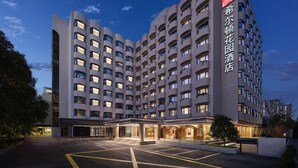Un hotel de varios pisos con diseño moderno, que destaca por su entrada con área cubierta y un estacionamiento al frente.