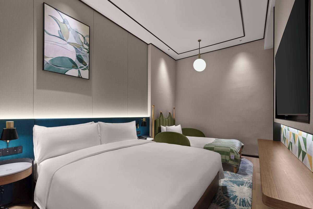 Una habitación de hotel moderna con una cama grande, una cama más pequeña, un escritorio y un televisor.