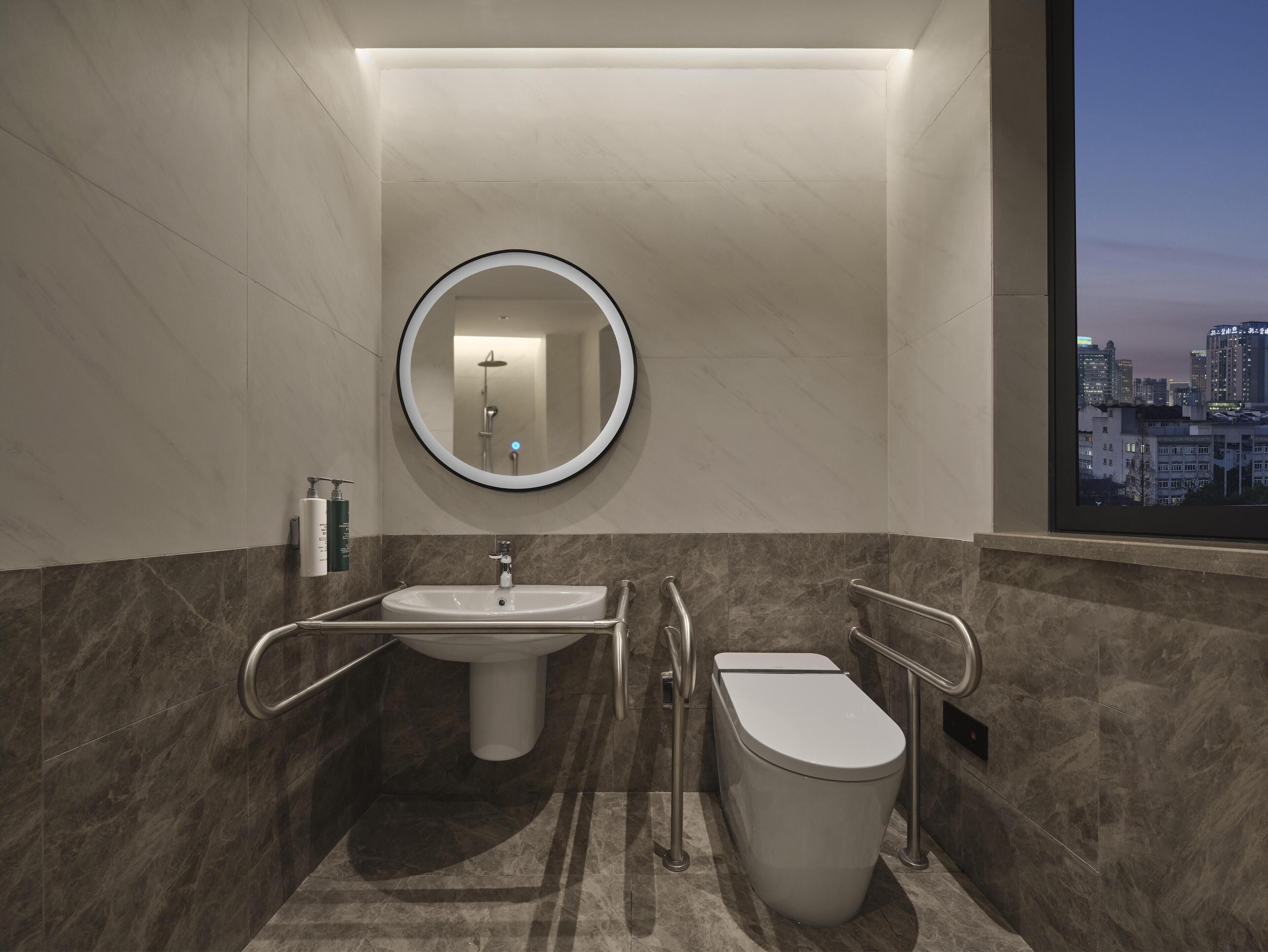 A modern bathroom with a round mirror, a sink, and a toilet.