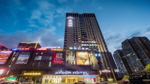 A hotel with a prominent sign for "ATOUR HOTEL" and multiple illuminated storefronts in the foreground. - Atour Hotel Binjiang Binwen Road Hangzhou (Hangzhou)