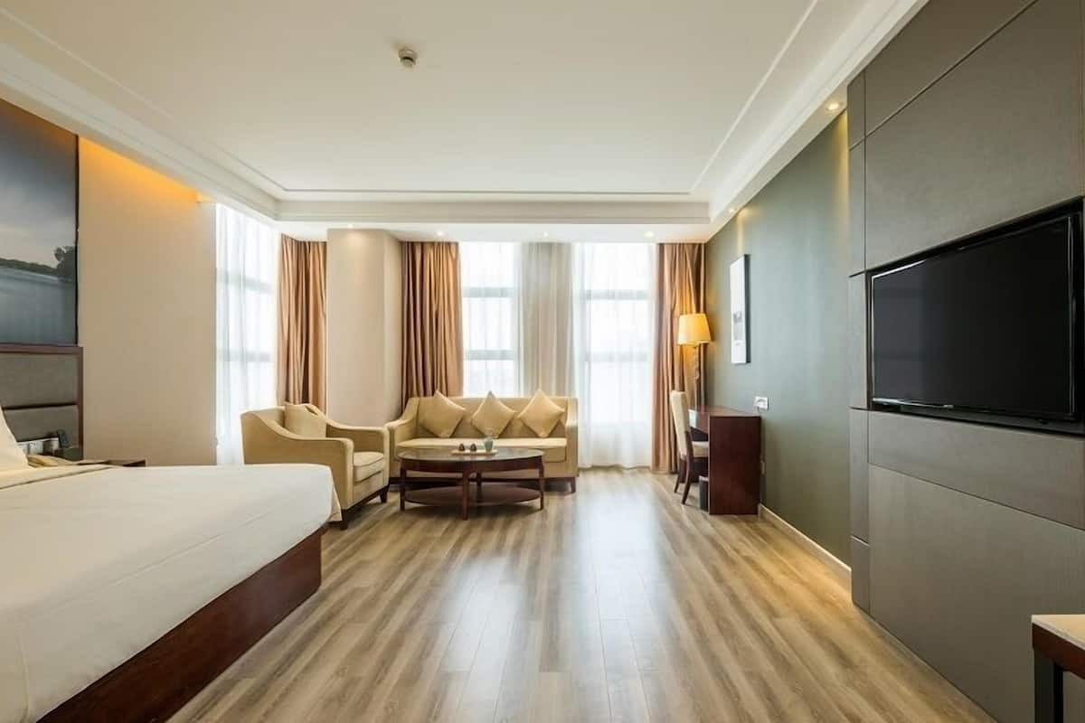 Ein Hotelzimmer mit einem großen Bett, einem Sofa, einem kleinen Tisch, einem Fernseher und einem Gemälde an der Wand.