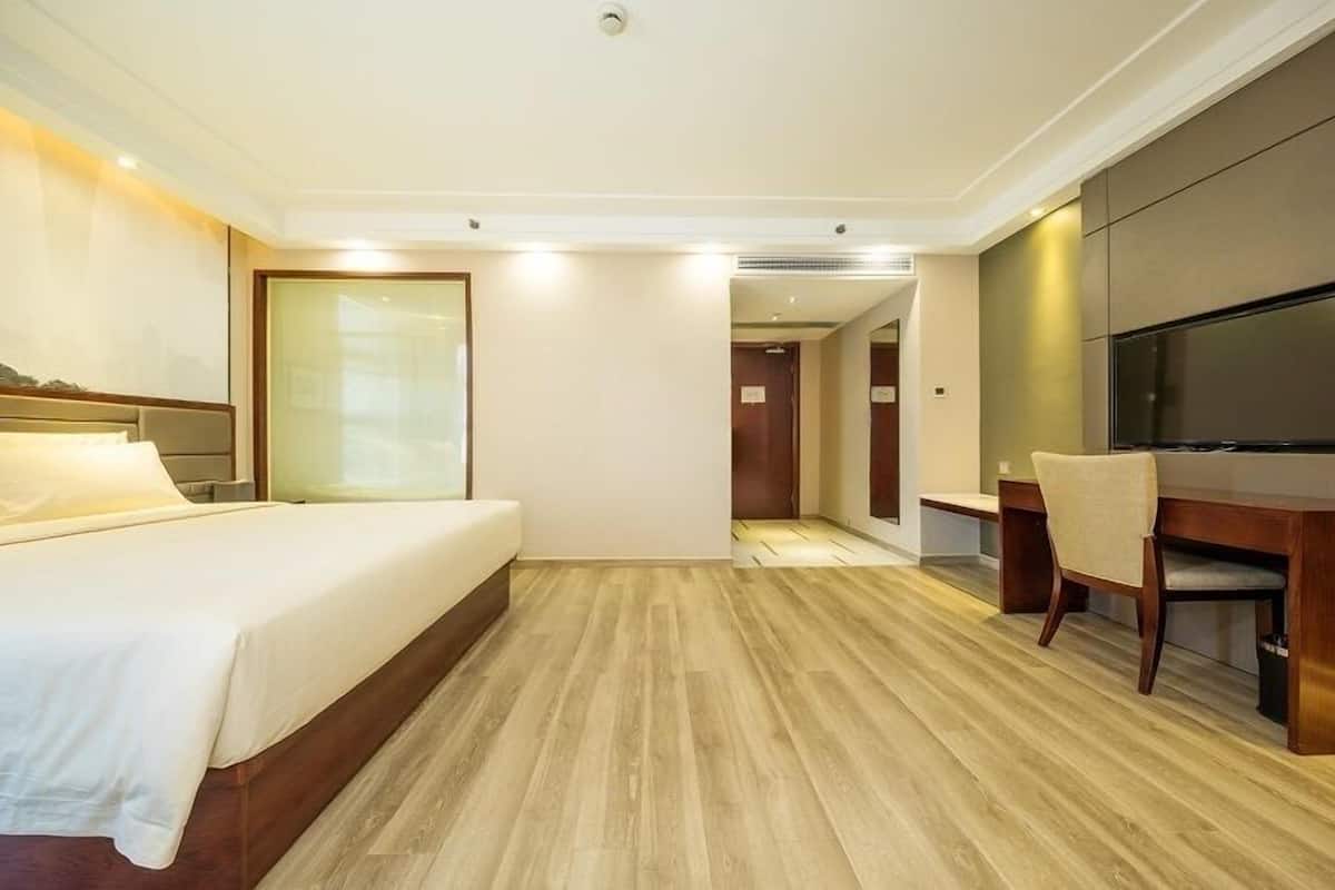 Ein Hotelzimmer mit Bett, Schreibtisch, Stuhl, Fernseher und Holzboden.