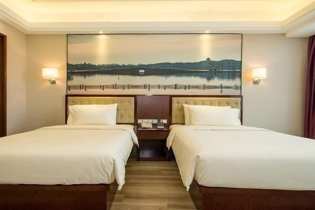 Ein Hotelzimmer mit zwei Betten, einem Nachttisch, einem Landschaftsbild und Blick auf ein Gewässer.