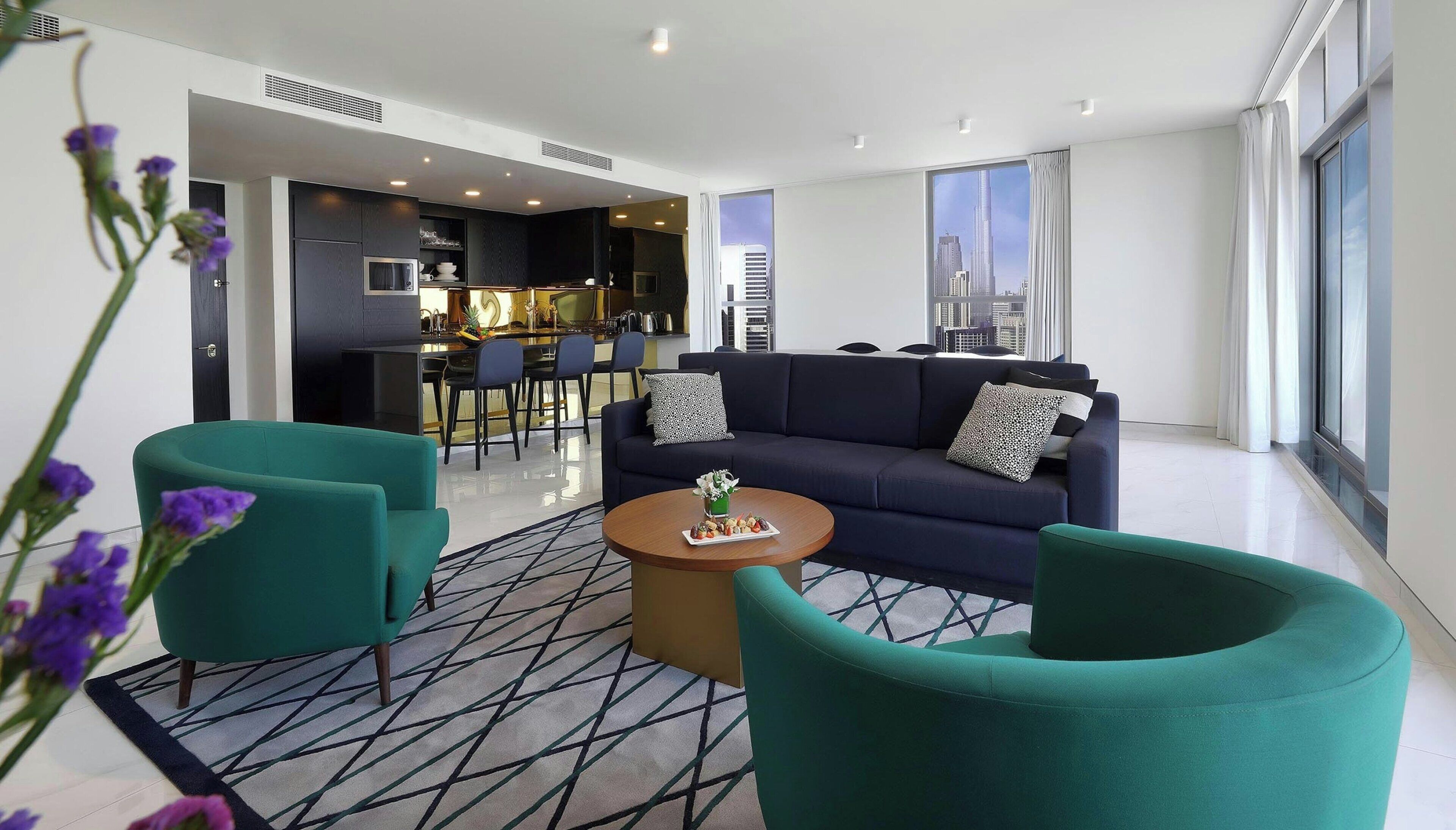 Una sala de estar moderna con un sofá, dos sillones color turquesa, una mesa de centro y una alfombra estampada.