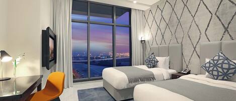 A hotel room with a large window, two beds, a desk, and a chair.
