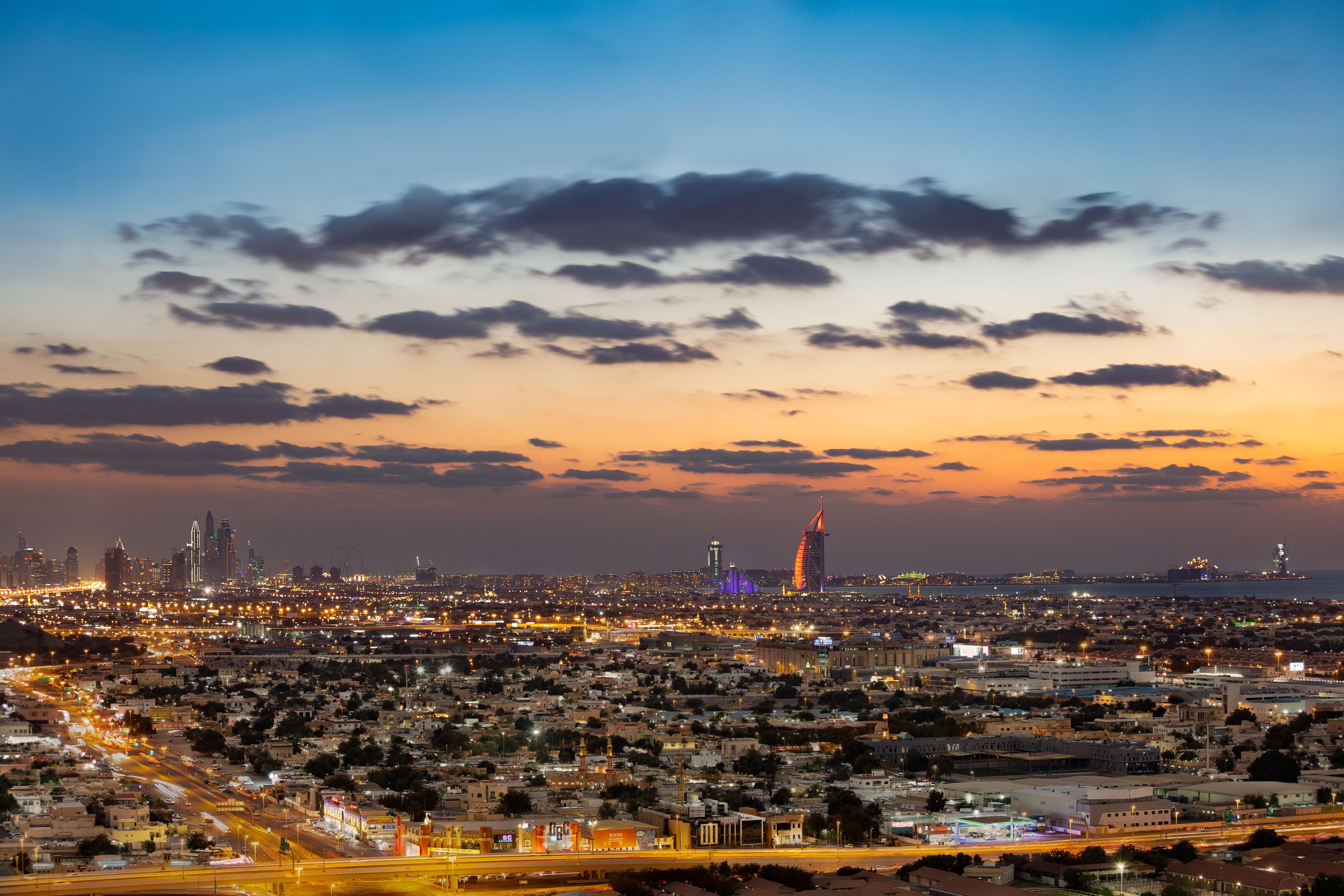 A cityscape at dusk with illuminated buildings and a prominent tower in the distance.