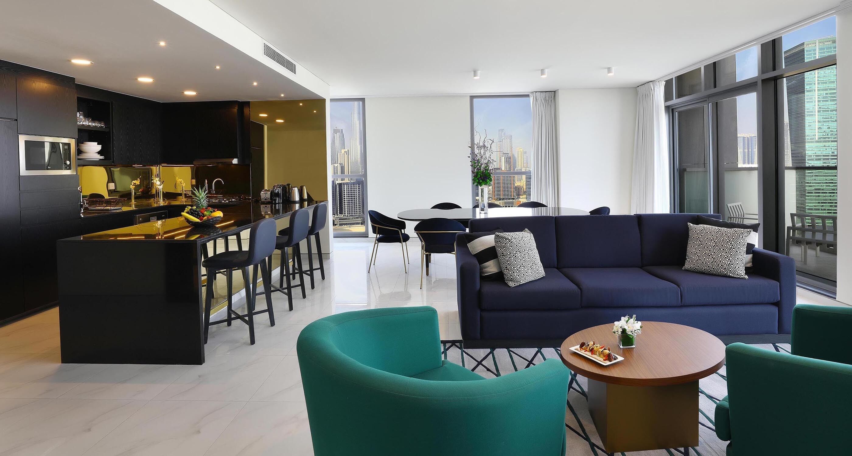 A modern living room with a sofa, chairs, a dining table, and a kitchen area.