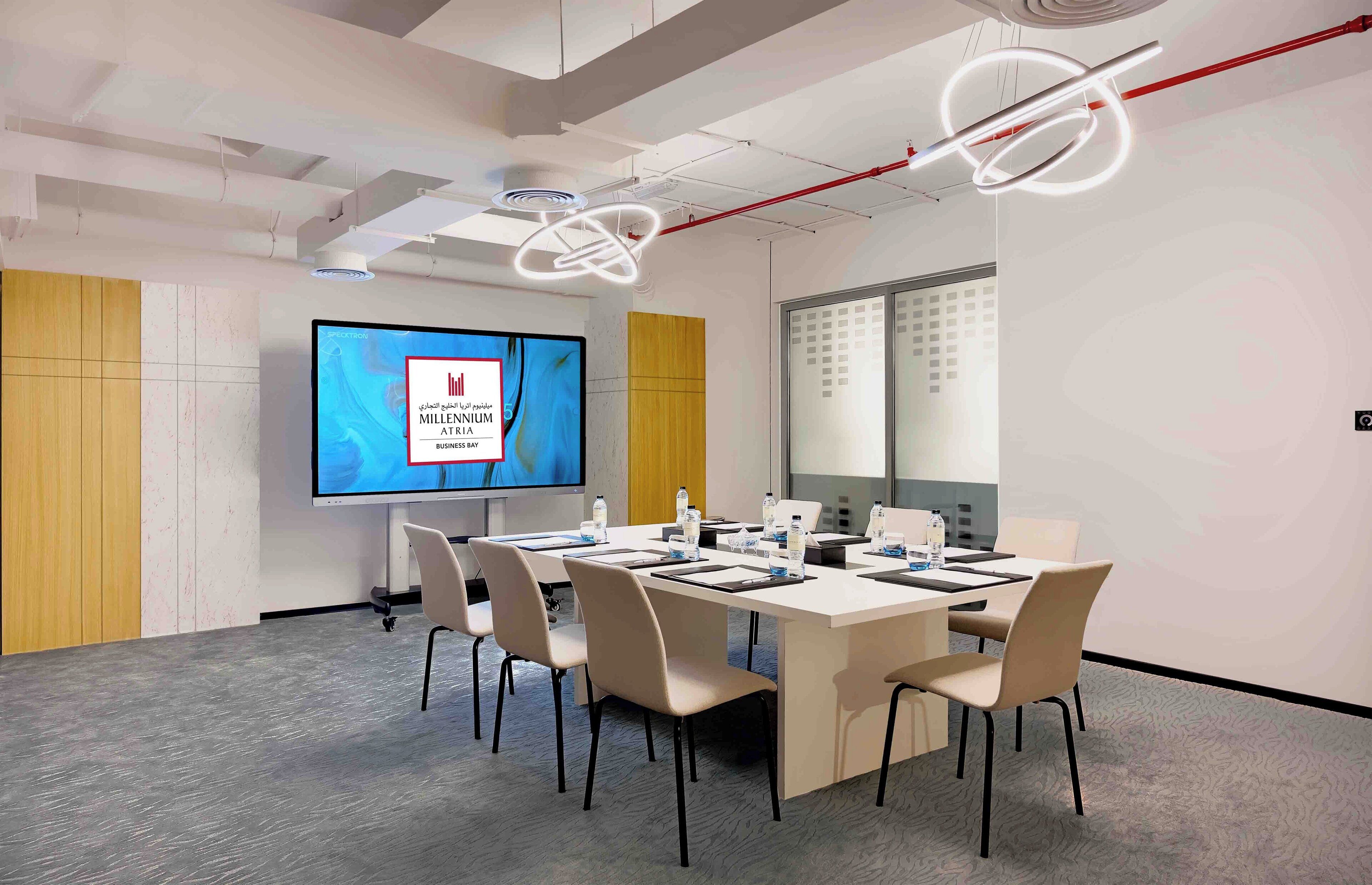 A modern conference room with a large screen displaying a presentation, a long table with chairs, and a glass partition wall.