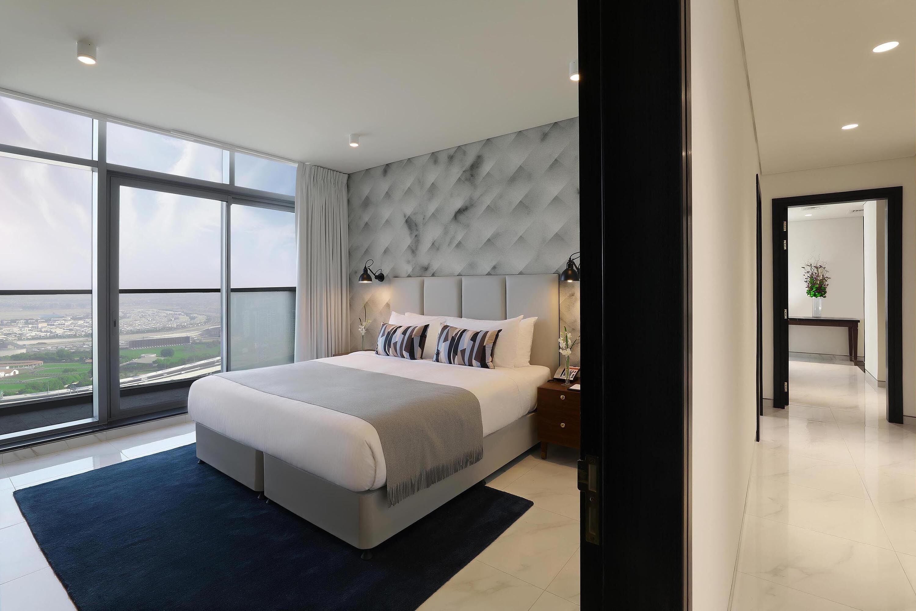 Een moderne slaapkamer met een groot bed, stadszicht door ramen van vloer tot plafond, en een wand met een marmerpatroon.