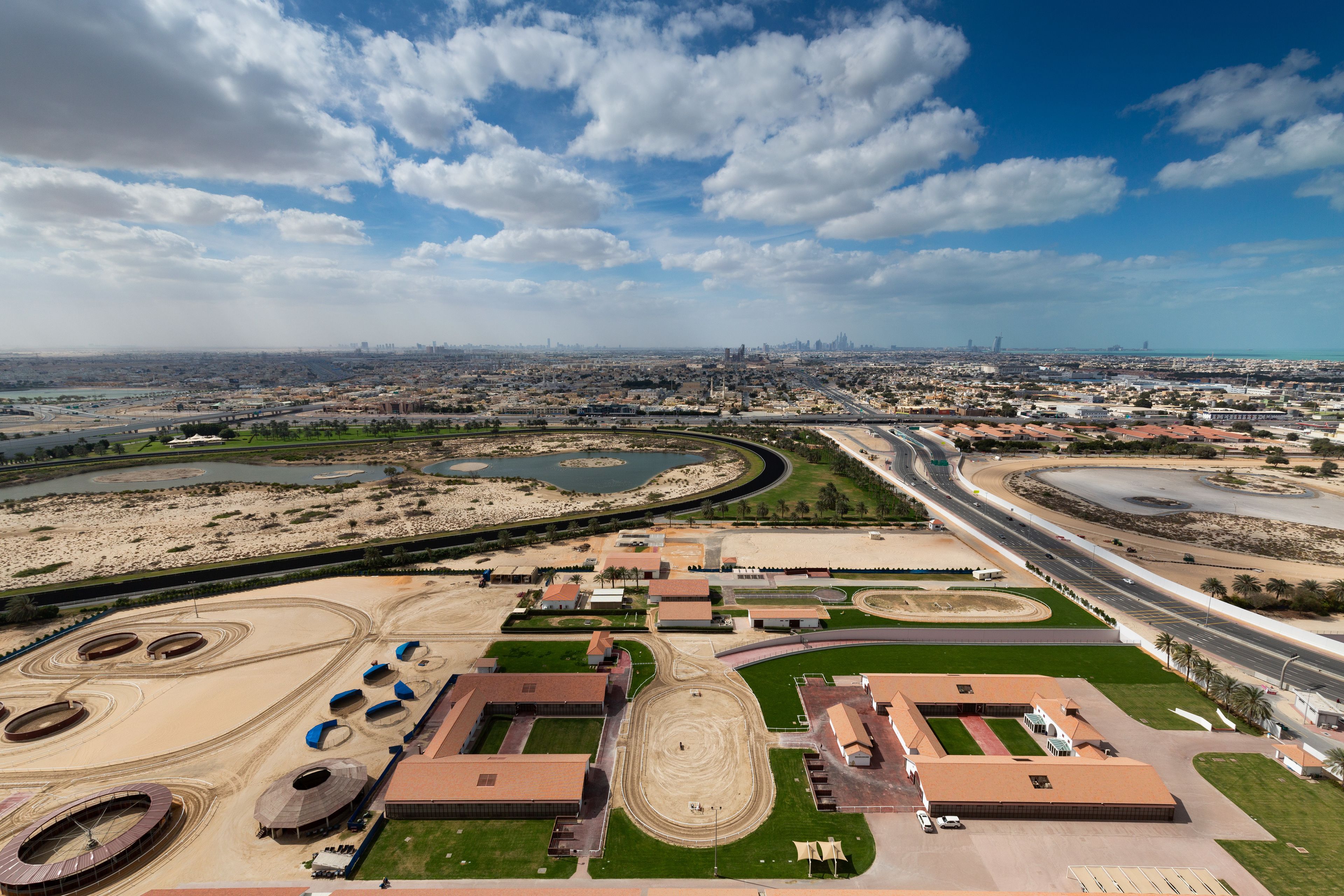 An aerial view of a large, undeveloped area with multiple circular structures, roads, and a distant city skyline.