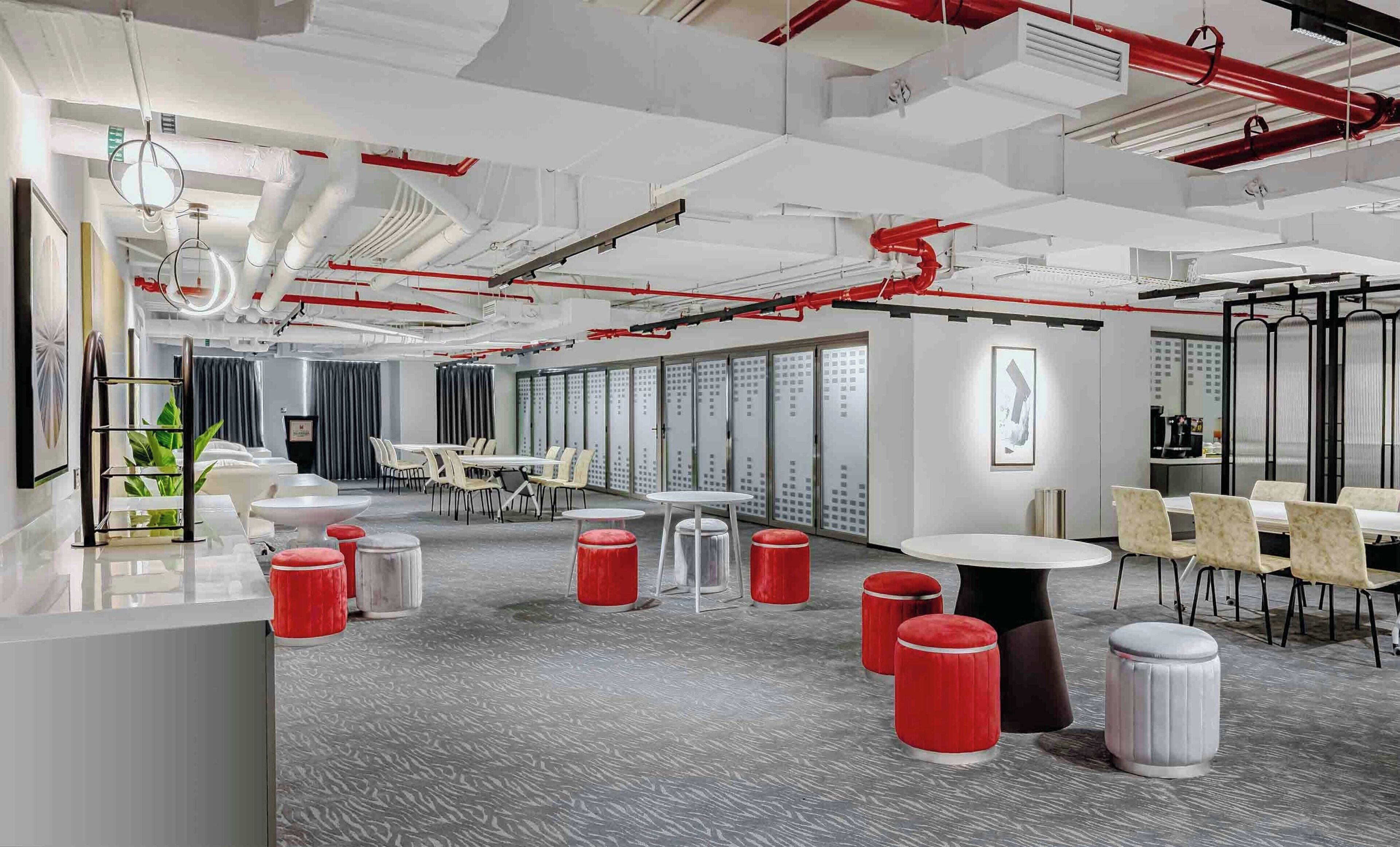 A modern office space with white walls, grey carpet, red accents, and a mix of tables and chairs.