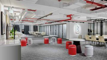 A modern office space with white walls, grey carpet, red accents, and a mix of tables and chairs.