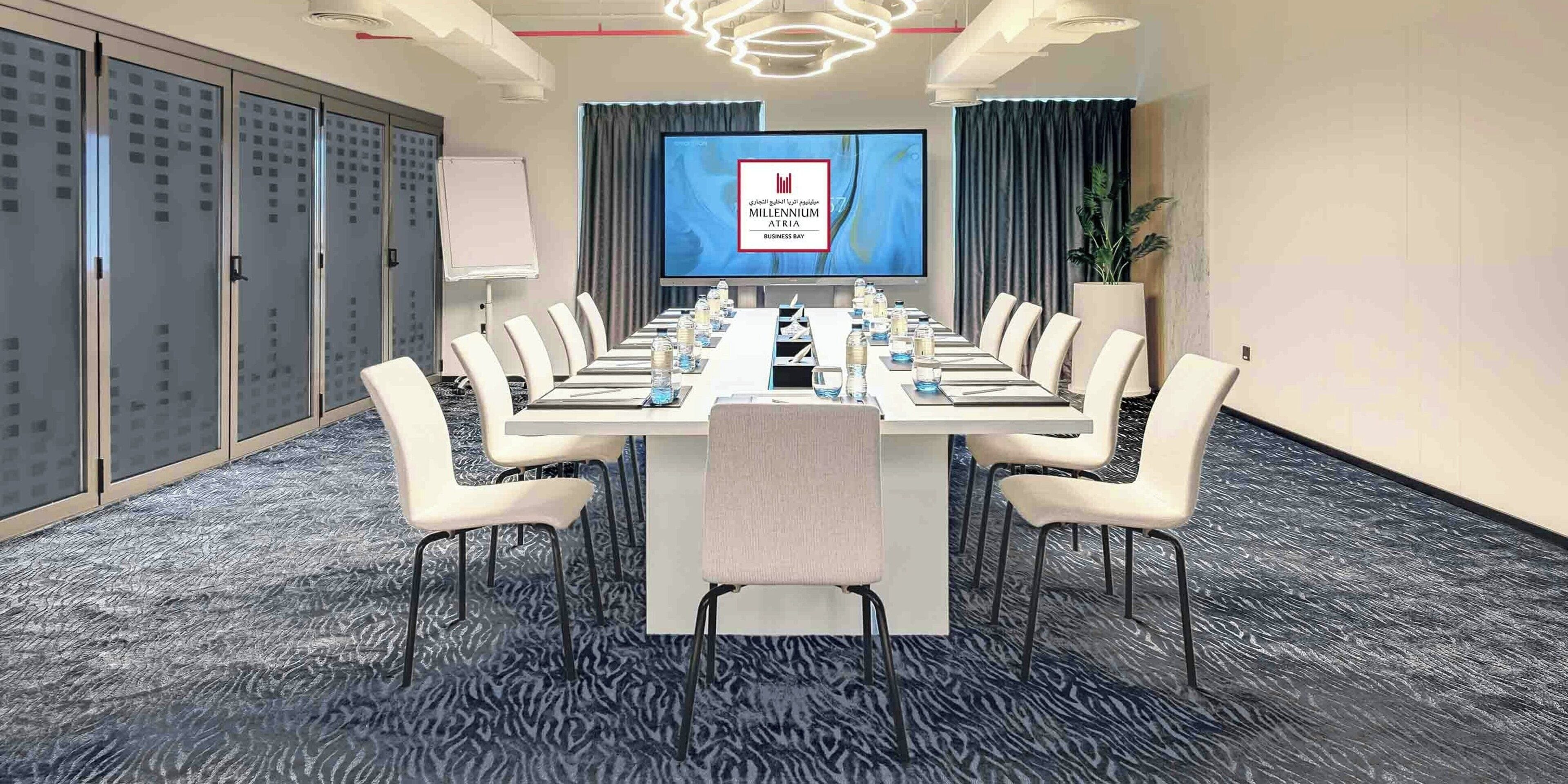 Un salón de conferencias con una larga mesa, sillas, una pantalla de proyector y una pizarra.