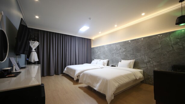 Een hotelkamer met twee bedden, een bureau met spiegel, een badjas en een groot raam met gordijnen.