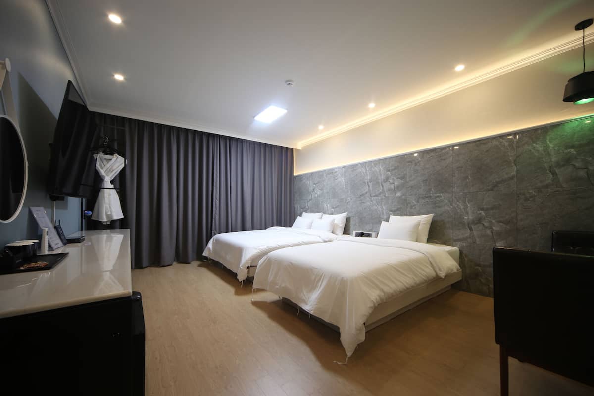 A hotel room with two beds, a desk with a mirror, a robe, and a large window with curtains.