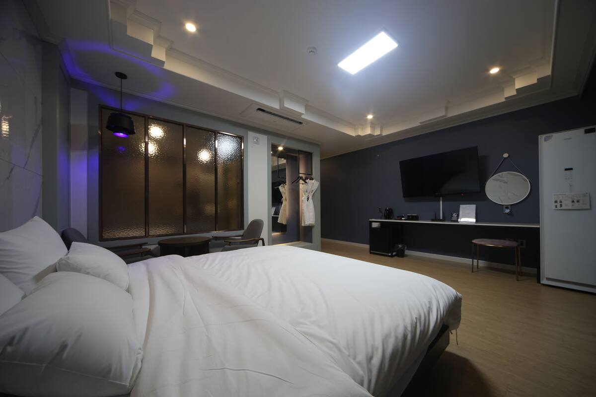 A modern hotel room with a large bed, a desk, a chair, and a TV mounted on the wall.