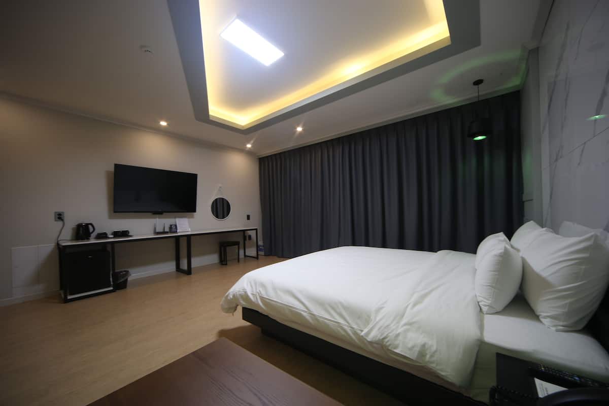 A modern hotel room with a large bed, a desk with a flat-screen TV, and a ceiling light fixture.