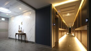 Een hotelgang met een marmeren muur, een donkere scheidingswand en een lange hal met verlichte plafondlampen.