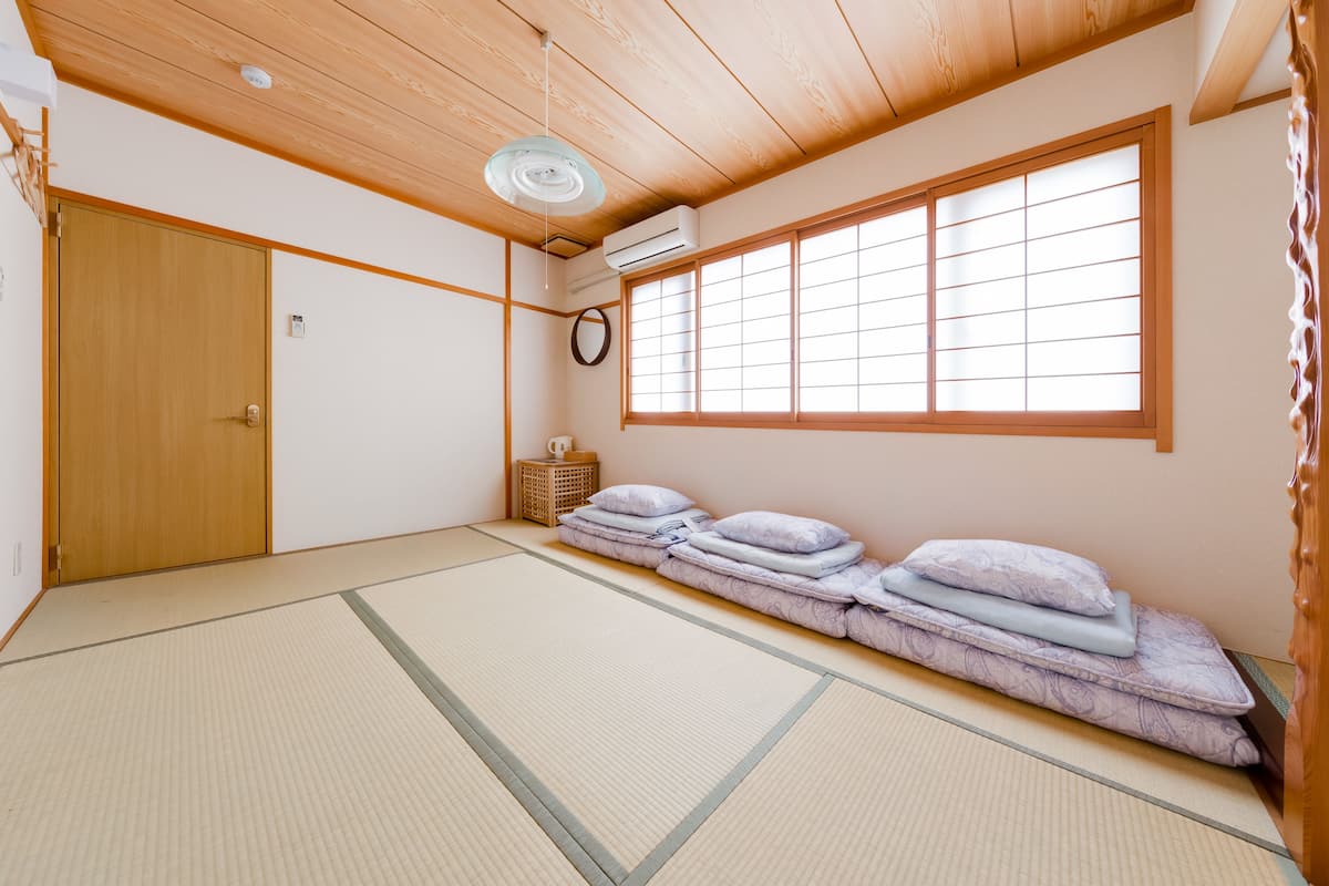 A traditional Japanese room with tatami flooring, a futon bed, a wooden door, and a large shoji screen window.