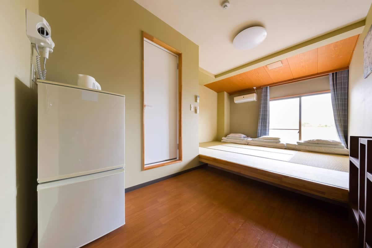 A compact room with a built-in bed, a small refrigerator, a wall-mounted heater, and a window with curtains.