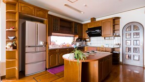 A kitchen with wooden cabinets, a stainless steel refrigerator, a central island with a plant, and a tiled backsplash. - Yolee Guest House (Izumisano)