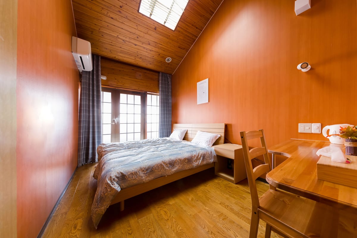 A bedroom with a wooden bed, a wooden desk, and a window with curtains.