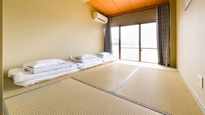 A room with tatami mats, a sliding door, and a stack of white towels. - Yolee Guest House (Izumisano)