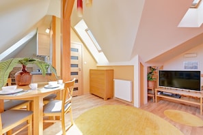 A modern loft bedroom with a sloped ceiling, skylight, wooden furniture, a flat-screen TV, and a dining area with a table and chairs. - Lion Apartments - Avocado (Sopot)